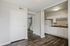 Modern apartment interior featuring a sleek kitchen with white cabinets and dark wood flooring, leading to an inviting staircase.