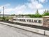 Inviting entrance to Misty Creek Village with lush greenery and elegant signage under a bright, blue sky.