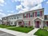 Charming townhouse with red shutters, manicured lawns, and elegant stone accents, set under a bright blue sky.
