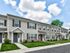 Charming townhouses with modern exteriors, surrounded by lush green lawns under a bright, cloudy sky.
