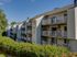 Sunlit apartment complex showcasing spacious balconies, surrounded by lush greenery, offering modern living with natural beauty.