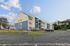 Charming apartment complex with modern blue and beige exterior, ample parking, and lush surroundings.