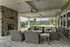 Inviting covered patio with cozy wicker seating and stone fireplace, overlooking a lush garden view.