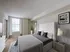 Elegant bedroom featuring a plush king-sized bed with tufted headboard, natural light from large windows, and tasteful decor.