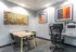 Modern office space with elegant decor, featuring a wooden table with four chairs, vibrant wall art, and a work area equipped with a printer and computer.