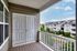 Charming balcony with white railing, overlooking serene residential buildings and lush greenery on a sunny day.