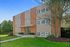 The exterior of The Greenbriar apartment building, a three-story brick building with balconies, surrounded by green lawns and trees.