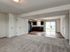 Open-concept living area with plush carpet, modern kitchen with dark wood cabinets, and large glass sliding doors leading to a bright outdoor space.