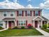 Charming two-story townhouse with red shutters and a welcoming entry, framed by well-maintained landscaping under a clear blue sky.