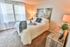 Inviting bedroom with plush white bedding, cozy ambiance, and natural light streaming through large windows.
