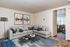 Elegant living room with a modern sectional sofa, chic artwork, and a glimpse into a cozy dining area filled with natural light.