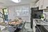 Modern kitchen and dining area featuring sleek cabinetry, granite countertops, and stylish grey chairs around a wooden table. Bright natural light filters through large windows, enhancing the inviting atmosphere.