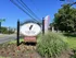 Charming entrance sign for Verona at Middle River with vibrant landscaping and 'Now Leasing' flags on a sunny day.