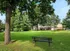 Serene apartment complex surrounded by lush greenery, featuring a spacious lawn and shaded seating area.