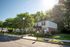 Charming residential building surrounded by lush greenery, featuring a well-maintained sidewalk and a welcoming entrance under a bright blue sky.