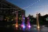 Vibrant evening scene of a lively community plaza featuring illuminated fountains and enchanting string lights, perfect for social gatherings.