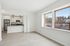 Bright and modern open-concept kitchen featuring sleek stainless steel appliances and elegant pendant lighting, adjacent to a spacious living area with large sunlit windows.