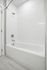 Modern bathroom featuring a sleek white bathtub with clean tile walls and a contemporary showerhead design.