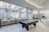Modern recreation room with a sleek pool table and ample natural light, featuring a stylish seating area beside large windows.