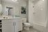 Modern bathroom featuring sleek white cabinetry, elegant tile flooring, and a stylish bathtub with shower. Accented by a large mirror and artistic wall decor.
