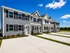 Modern and inviting row of townhouses with elegant design, featuring neatly manicured lawns and expansive driveways under a clear blue sky.