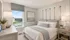 Bright and cozy bedroom with elegant decor, featuring a plush bed with soft blue and white linens, warm ambient lighting, and a scenic window view.