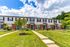 Charming townhouse row with brick facade, vibrant green doors, and lush landscaping under a bright blue sky.