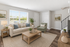 Bright and airy living room with modern furnishings, cozy couch, elegant armchair, and abundant natural light from large windows.
