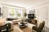 Inviting living room with modern decor, featuring a comfy beige sectional sofa, stylish coffee table, and large TV against a sunlit backdrop.