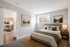 Elegant bedroom with a plush bed, soft lighting, and serene artwork, leading to a cozy living room with stylish decor and warm wooden floors.