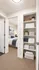 Inviting hallway with plush carpet leads to a cozy bedroom, featuring crisp white linens and tasteful decor. Organized storage area with neatly folded towels and elegant decor accents enhance the space's charm.