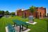 Charming outdoor space featuring lush green lawn, brick building backdrop, picnic tables, and a barbecue grill for perfect gatherings.