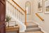 Inviting entryway with warm wooden accents, featuring a welcoming sign on a console table, elegant staircase, and serene wall art.