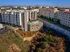 Modern apartment complex with rooftop pool, surrounded by scenic views and vibrant greenery in an urban setting.