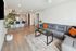 Modern open-concept living room with stylish gray sectional, vibrant orange pillows, and sleek kitchen with bar seating.