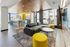 Modern apartment lounge with sleek gray sofa, vibrant yellow seating, and chic kitchen featuring stylish bar stools and pendant lighting.