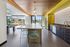 Modern communal kitchen with sleek island seating, geometric backsplash, and bright yellow accents, opening to a vibrant outdoor lounge.