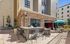 Modern outdoor patio featuring a stone countertop bar with high stools, adjacent to a stylish grill area, under a vibrant blue umbrella.