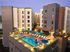 Modern apartment complex featuring a luxurious rooftop pool area with comfortable lounge chairs and vibrant blue umbrellas, perfect for relaxation and leisure.