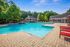 Inviting outdoor pool area with vibrant red loungers, surrounded by lush greenery and a spacious patio.