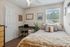 Bright and cozy bedroom featuring a plush bed, stylish decor, and a convenient workspace with natural light streaming through a large window.