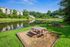 Scenic lakeside view of modern apartments with inviting picnic area, surrounded by lush greenery under a clear blue sky.