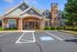Charming residential building with inviting stone facade and manicured landscaping, featuring accessible parking space and bright blue sky.