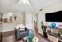 Inviting apartment living area with elegant decor, featuring a cozy armchair, modern shelving, and a sleek entertainment center under a ceiling fan, leading to a bright bedroom with plush carpeting.
