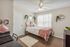 Charming bedroom with cozy decor, featuring a comfy bed with pink accents, elegant wall shelves, and ample natural light.