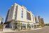 Modern multifunctional building with sleek architecture, featuring commercial spaces on a vibrant street corner under a clear blue sky.