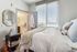 Cozy bedroom with a plush bed, large window with blinds, and a sleek modern design. Adjacent bathroom visible through open door, adding to the seamless elegance of the apartment.