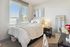 Inviting bedroom bathed in natural light, featuring a cozy bed with plush, white bedding, elegant decor, and fresh flowers on a stylish nightstand.