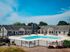 Charming residential complex featuring a sparkling swimming pool, surrounded by inviting lounge chairs and a stylish clubhouse, set against a backdrop of lush greenery and blue skies.