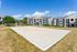 Inviting apartment complex with modern gray and white buildings, featuring a pristine sand volleyball court under a vibrant blue sky.